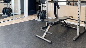 Un gimnasio con equipo de levantamiento de pesas, una banca y un espejo que refleja el equipo.