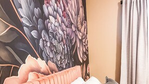 Una cama con cabecera rosa, almohadas blancas y grises, y un mural floral en la pared de fondo.