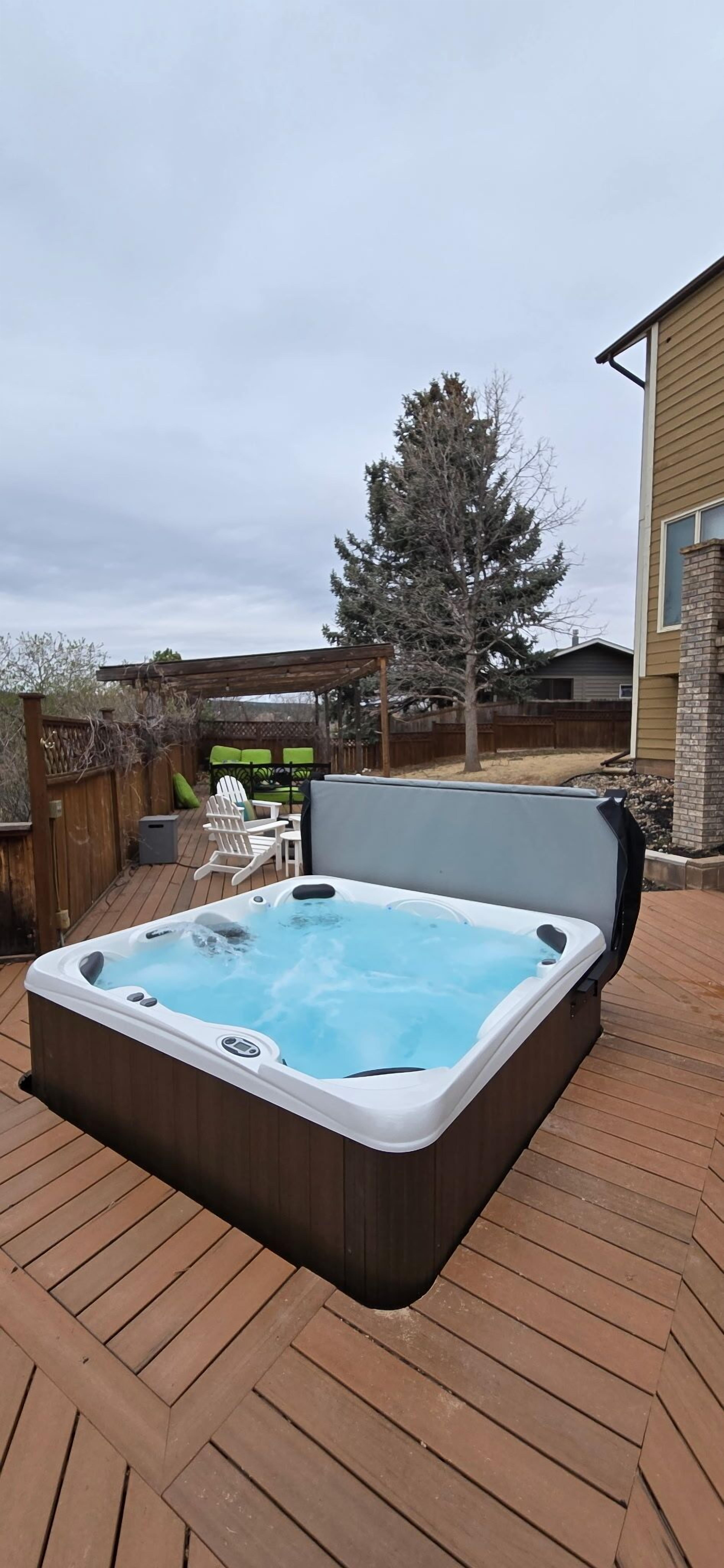 A hot tub on a wooden deck with a wooden fence and a tree in the background.