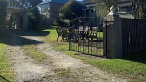 Un quartier résidentiel avec une allée en gravier, une entrée fermée par un portail et un espace repas aménagé avec du mobilier d’extérieur.