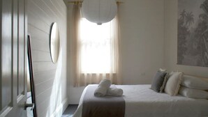 Une chambre à coucher avec un lit, un grand miroir, une fenêtre avec des rideaux et un luminaire fixé au mur.