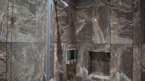 Une cabine de douche en marbre équipée d’un pommeau de douche à main et d’un robinet mural.