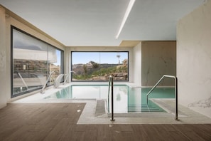 En moderne swimmingpool indendørs med glasvægge, udsigt til stengrund og trægulv.