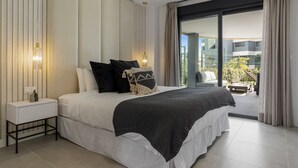 A modern bedroom with a large bed, a bedside table, and a view of a balcony with outdoor furniture. - La Brisa | Pool - terrace - gym (Estepona)