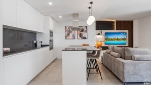 A modern kitchen with a central island, a dining area with a sofa and bar stools, and a living area with a large flat-screen TV. - La Brisa | Pool - terrace - gym (Estepona)
