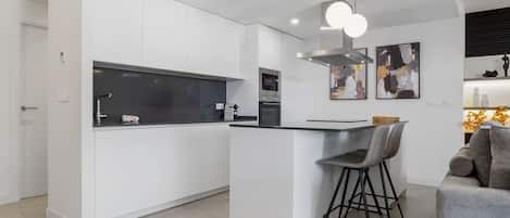 A modern kitchen with white cabinetry, a central island with bar stools, and a dining area with a sofa.