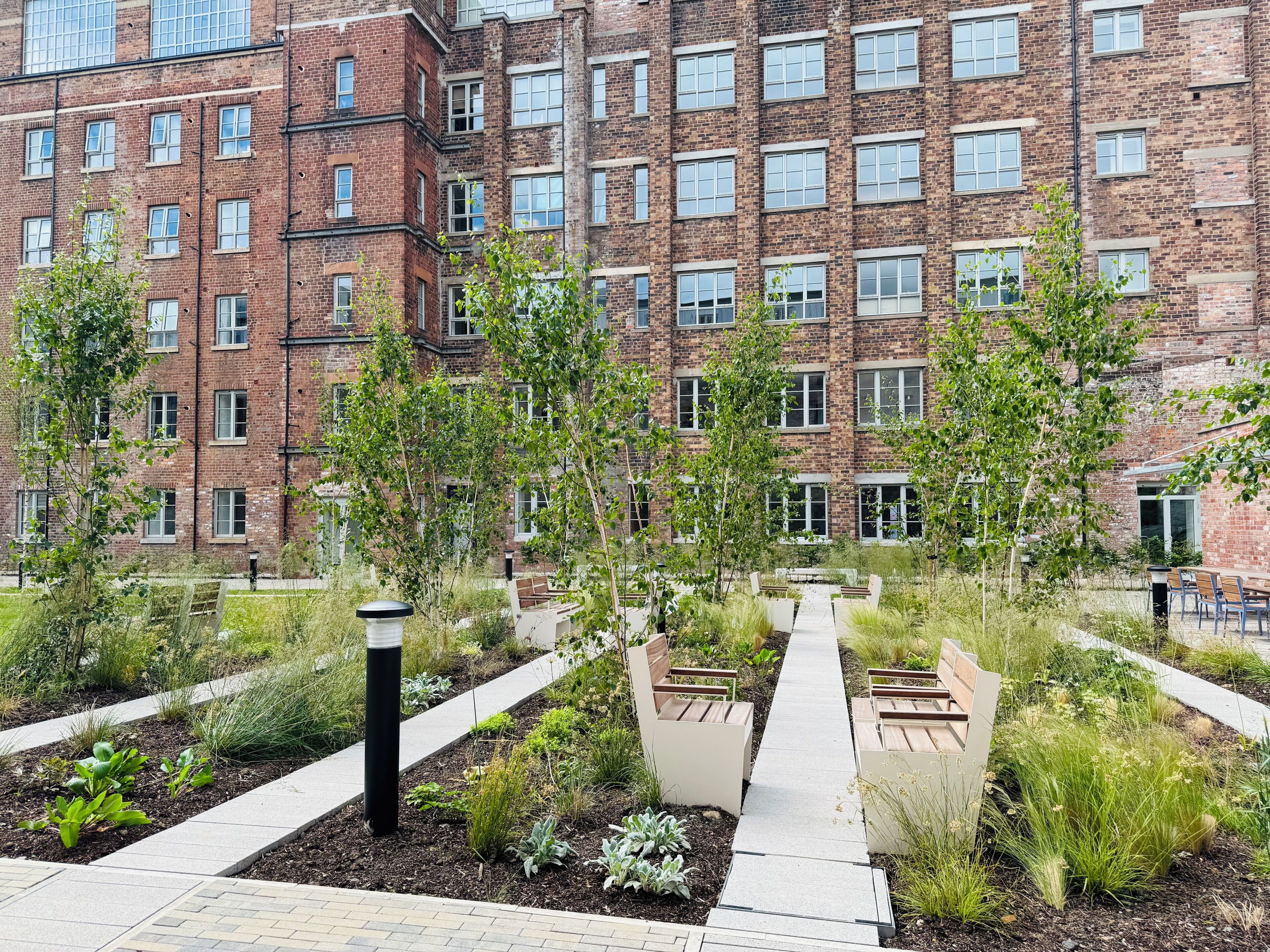A multi-story brick building with a courtyard featuring pathways, benches, and greenery.