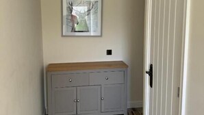 A hallway with a grey cabinet, a framed picture on the wall, and a white door. - Glass Street Apartment (Glenrothes)