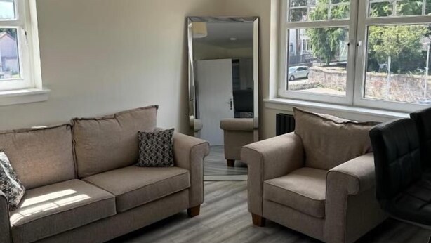 A living room with a beige sofa, two armchairs, a coffee table, and a large mirror. - Glass Street Apartment (Glenrothes)