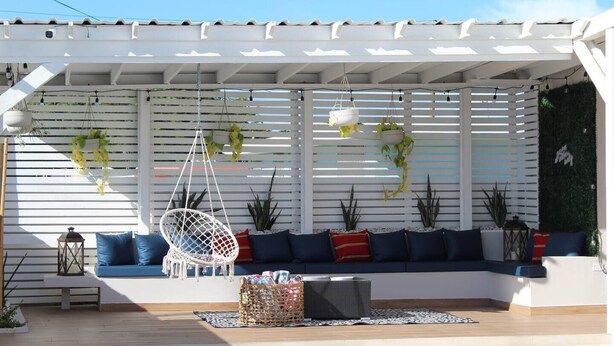 A covered outdoor seating area with a white pergola, hanging plants, and a wicker basket.