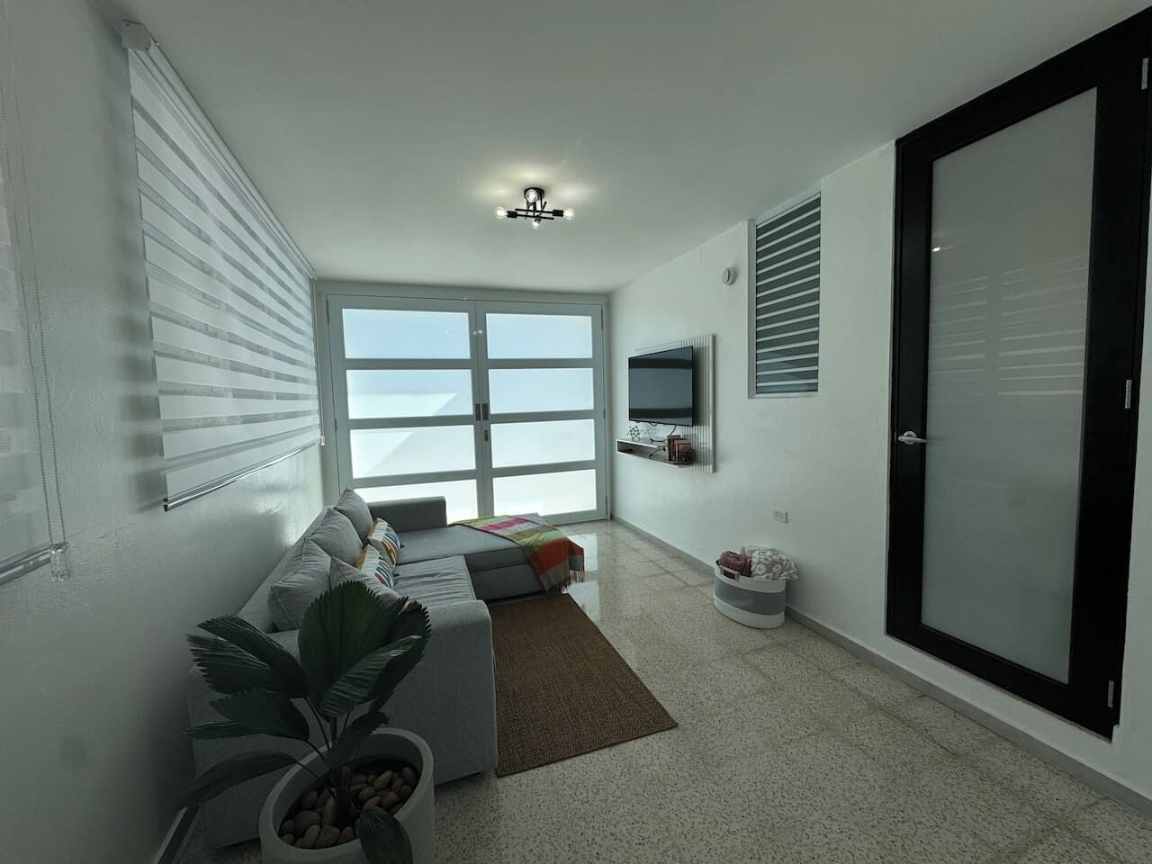 Ein modernes Wohnzimmer mit einer Couch, einem Couchtisch, einem an der Wand montierten Fernseher und einer Schiebetür aus Glas.