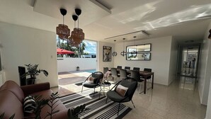 A modern living room with a sofa, chairs, and a dining area. There is a large window and a view of the outside.
