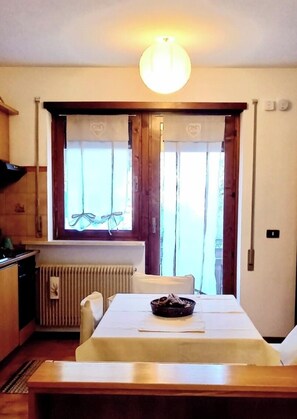 Un comedor con una mesa dispuesta para dos personas, un radiador, una ventana con cortinas y una lámpara en el techo.