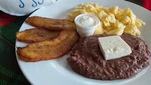 A plate with fried plantains, scrambled eggs, beans, and a piece of cheese. - Hotel Playa Bonita (Tela)