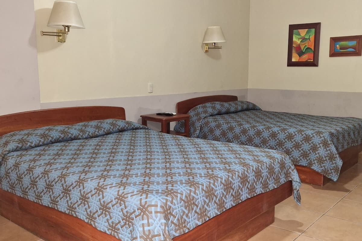 Una habitación con dos camas, cada una con colcha estampada, una mesita de noche y lámparas de pared.