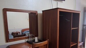 A room with a wooden desk, chair, and a wardrobe with shelves. A television is mounted on the wall above the desk. - Hotel Playa Bonita (Tela)