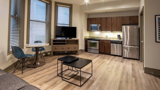 Un espacio habitable compacto con kitchenette, una zona de comedor con mesa y sillas, y una sala de estar con sofá.