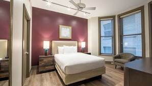 Habitación de hotel con una cama grande, dos lámparas de noche, un ventilador de techo y una ventana con persianas.