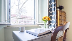A desk with a book and a mug, a vase with sunflowers, and a window with a view of buildings. - Elegantis.it La ParioLina Apartment (Roma)