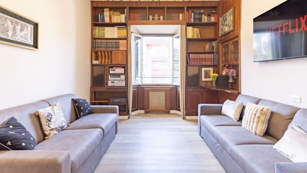 A living room with two sofas, a bookshelf, a television, and a window. - Elegantis.it La ParioLina Apartment (Roma)