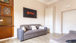 A living room with a grey sofa, a wall-mounted Netflix sign, a wooden cabinet, and a white wardrobe. - Elegantis.it La ParioLina Apartment (Roma)