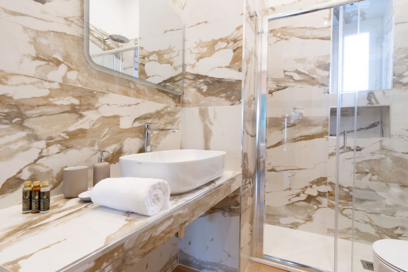 Un bagno con un mobile lavabo in marmo, box doccia in vetro e lavandino bianco.