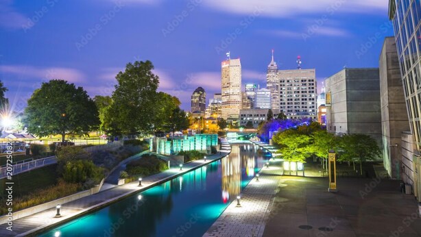 Une vue nocturne d’une ville, avec une rivière, des bâtiments illuminés et un pont.