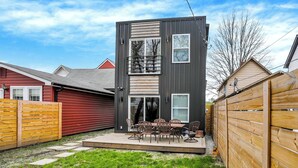 Un bâtiment moderne à deux étages, doté d’un balcon, d’une terrasse avec mobilier d’extérieur et d’une clôture en bois.