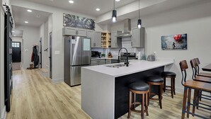 Une cuisine moderne dotée d’un grand îlot central, d’appareils électroménagers en acier inoxydable et de tabourets de bar en bois.