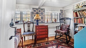 A room with a wooden floor, a red dresser, a rocking chair, a patterned rug, and a bookshelf filled with books. - 4 bedroom gorgeous home in Fanø (Fanø)