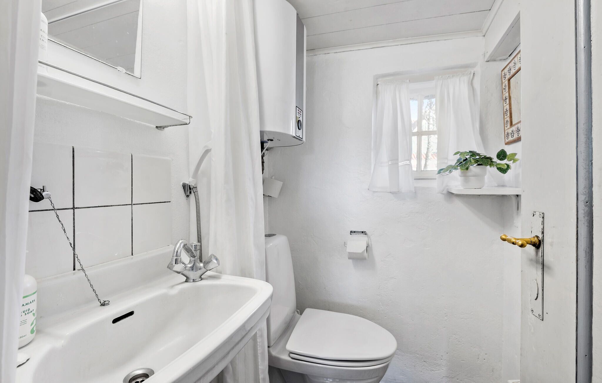A small, white bathroom with a bathtub, toilet, and a window with curtains.