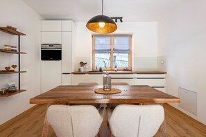 Una cocina moderna con horno empotrado, mesa de comedor de madera y una lámpara colgante.