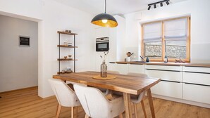 A modern kitchen with white cabinets, a wooden dining table, and a pendant light. - Apartment 'Jan's  Am See' with Lake View, Balcony and Wi-Fi (Pracupola)