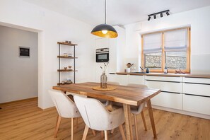 Une cuisine moderne avec des meubles blancs, une table à manger en bois et un luminaire suspendu.