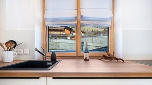 A kitchen with a wooden countertop, a sink, a wine bottle, and a view of a building and landscape through a window. - Apartment 'Jan's  Am See' with Lake View, Balcony and Wi-Fi (Pracupola)