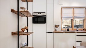 A modern kitchen with white cabinets, a built-in oven, wooden shelves, and a window with white curtains. - Apartment 'Jan's  Am See' with Lake View, Balcony and Wi-Fi (Pracupola)