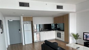 A modern kitchen with white cabinets, a black countertop, and a built-in oven. There is a black leather sofa and a small table with a plant.