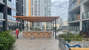 An outdoor seating area with a wooden pergola, a bench, and a planter with plants.