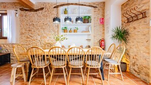 Un coin repas avec un mur en pierre, des chaises en bois, une table, des lampes suspendues et une plante en pot.