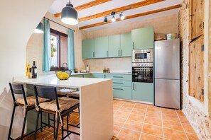 A kitchen with a central island, a sink, and a stove. There are chairs and a table with a bowl of fruit.