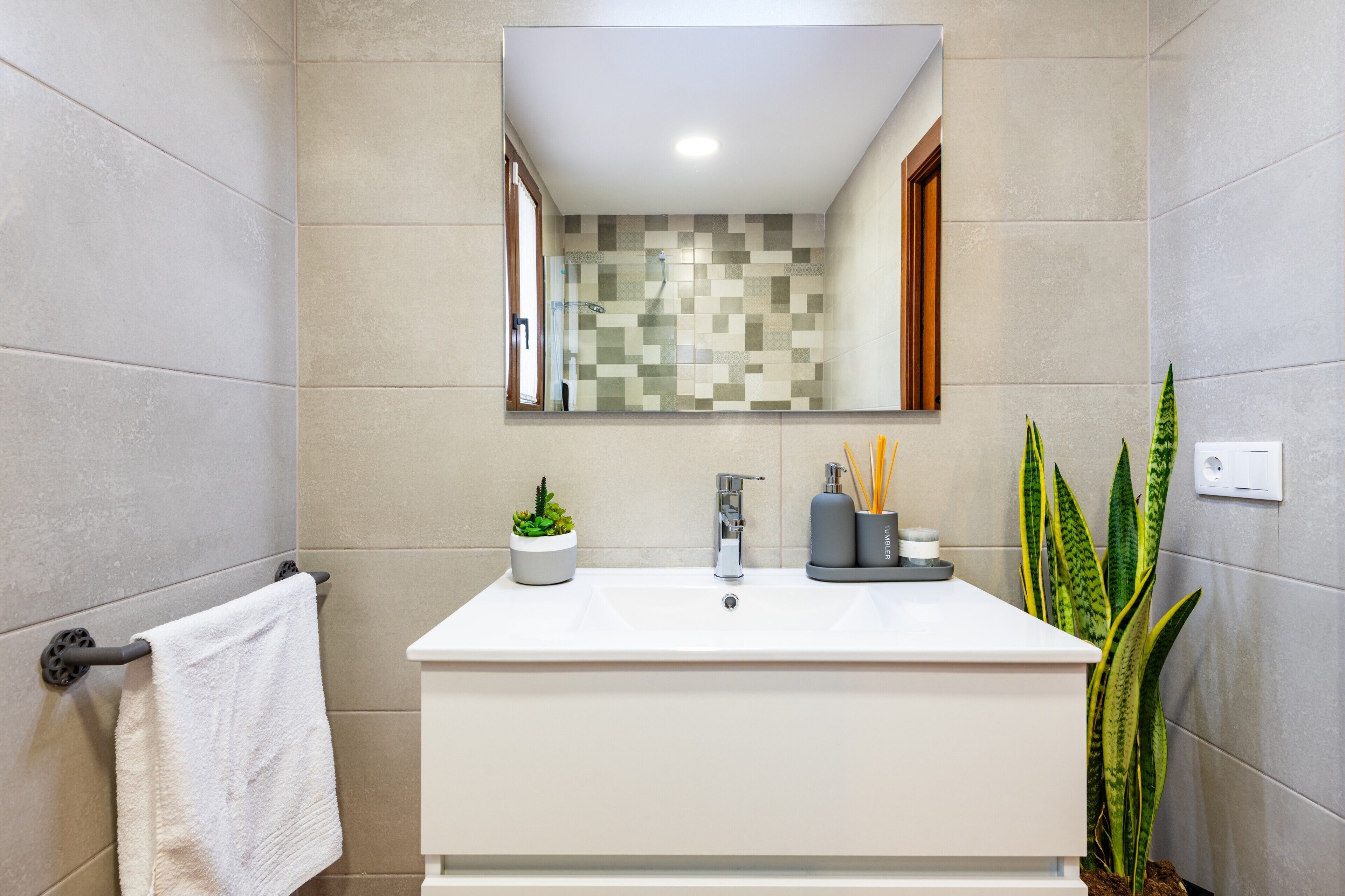 A bathroom with a white sink, a mirror, a potted plant, and a towel rack.