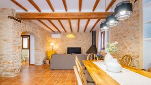 Un intérieur rustique avec des murs en pierre, des poutres en bois, une table à manger avec des chaises, un canapé et un téléviseur.