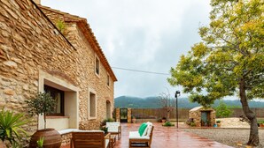 Un bâtiment en pierre doté d’une terrasse, de sièges en plein air et de plantes en pot.