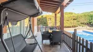 A covered patio with a table and chairs, a pool, and a wooden fence.
