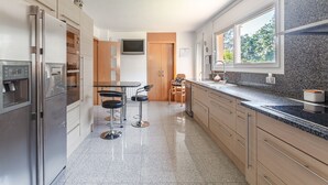 A modern kitchen with stainless steel appliances, a dining area with bar stools, and a large window providing natural light.