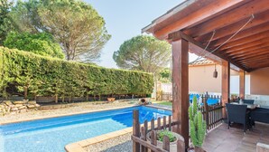 A swimming pool with a wooden deck, a pergola, and a fenced area with potted plants.