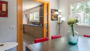 A dining area with a table, chairs, a vase with flowers, and a view of the kitchen and outdoors.