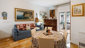 A living room with a sofa, a dining table, a guitar, and a piano.