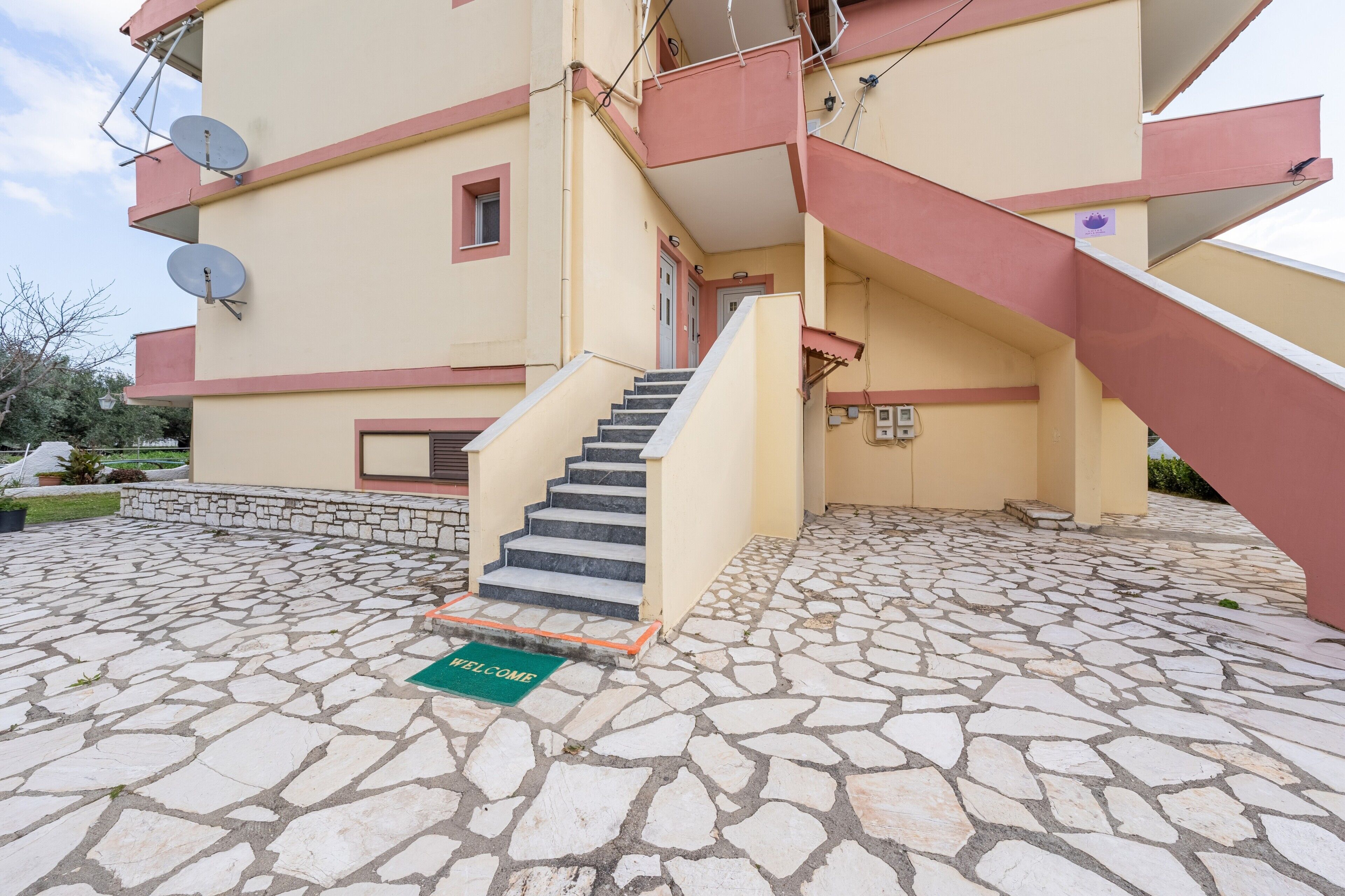 Un edificio con ingresso lastricato in pietra, una scala e antenne paraboliche sulla facciata.