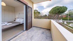 A bedroom with a bed, a sliding door, and a balcony with a view of trees and a house. - Apartment 'Lotus 1' with Sea View, Wi-Fi and Air Conditioning (Corfu)